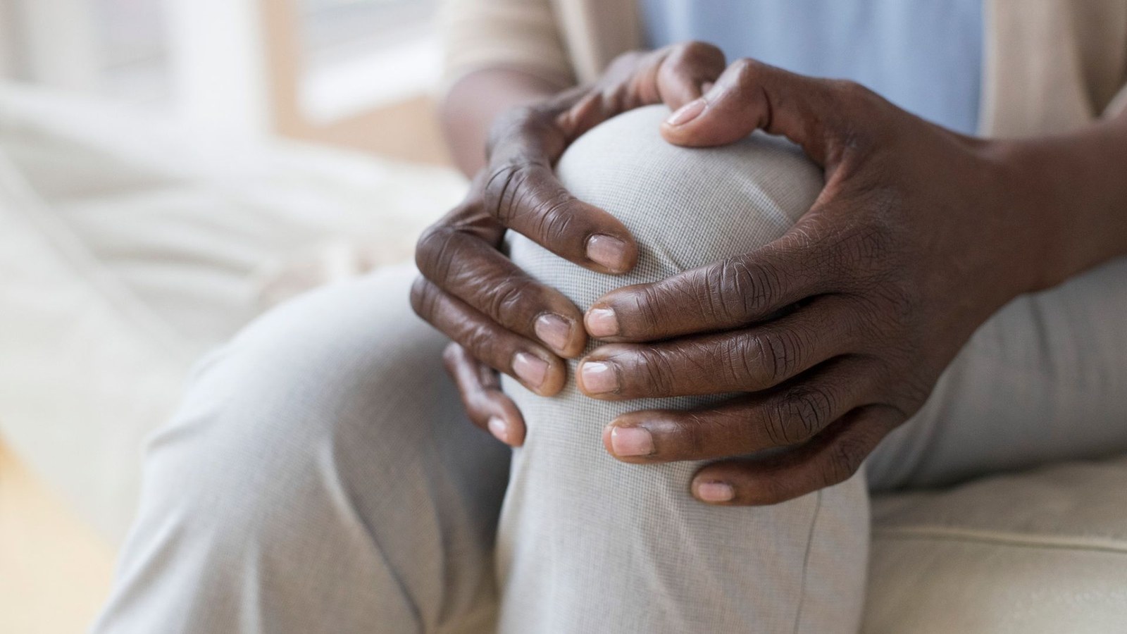 A close up of a person wearing white pants massaging their knee.