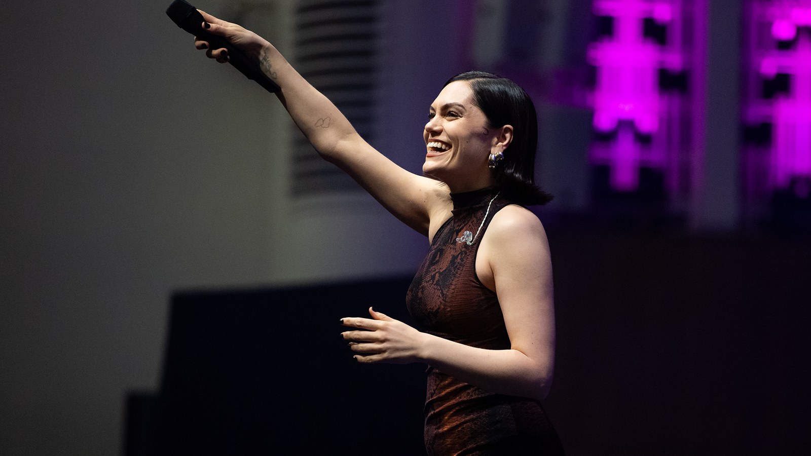 A woman wearing a maroon dress holds a microphone