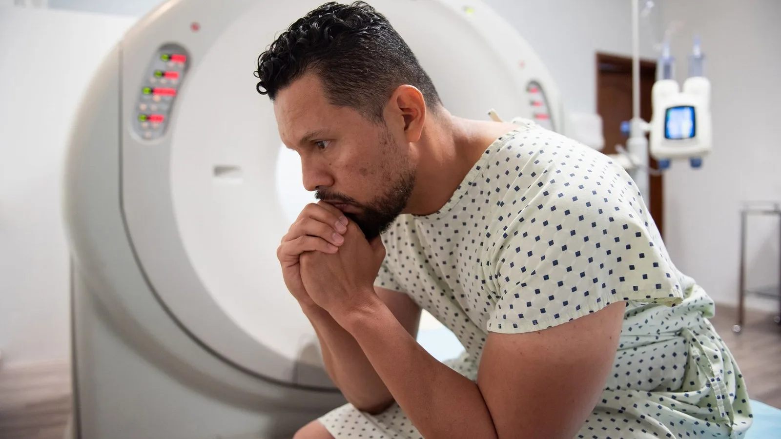 A man in a white dotted hospital gown sits in front of an MRI machine