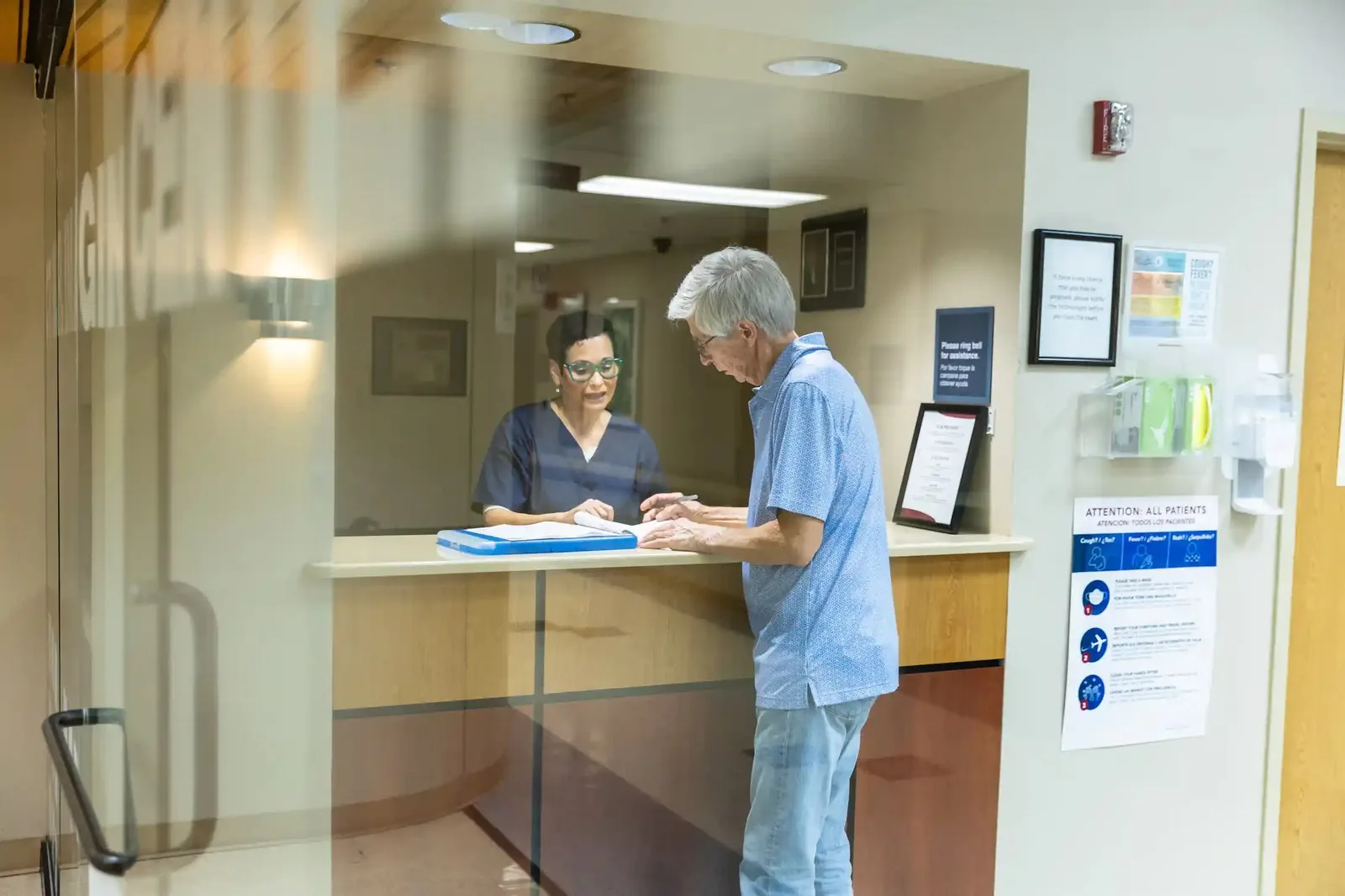 Older male patient signs forms at reception desk of medical office