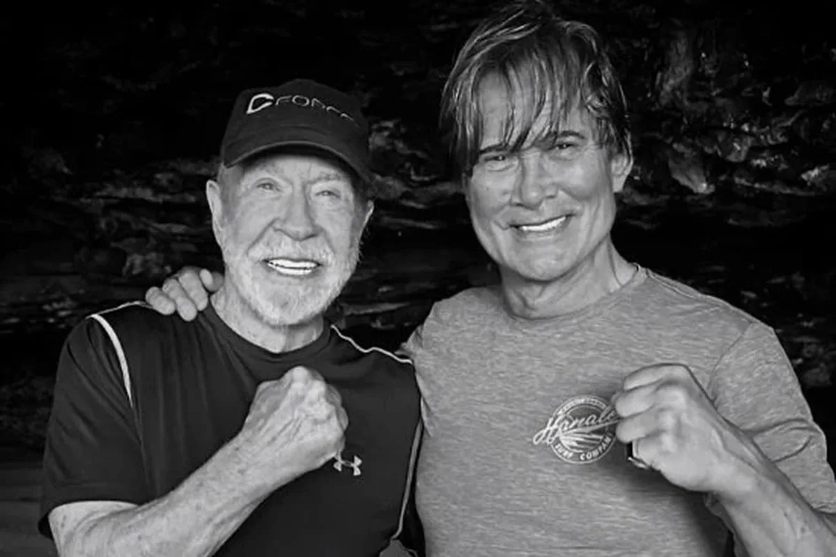 Black and white image of two men with their arms around each others' shoulders holding a fist up to the camera