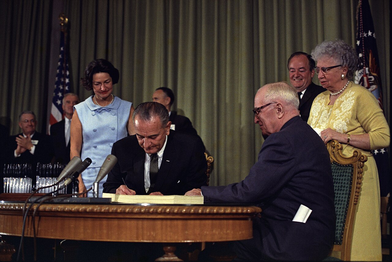 Lyndon B. Johnson signing the Medicare amendment (July 30, 1965). Former president Harry S. Truman (seated) and his wife, Bess, are on the far right.